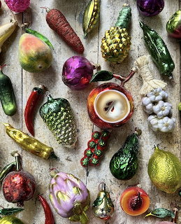 Colorful vintage glass ornaments shaped like fruits and vegetables arranged in rows on grey surface