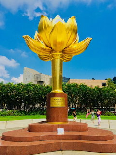 Golden lotus flower monument in plaza under blue sky with people