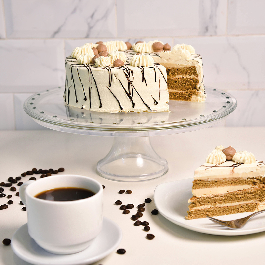 Layered moka cake on a glass stand with a coffee cup and a slice on a white plate