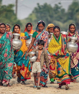 Group of women in colorful saris carrying metal water pots along a dusty road with a child