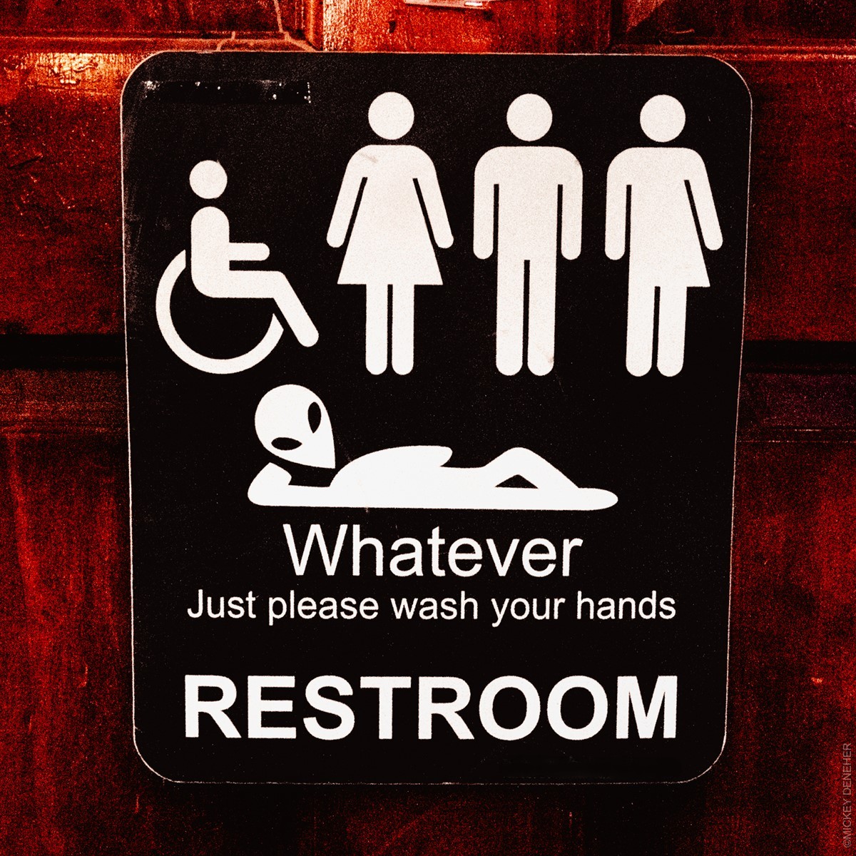 Inclusive restroom sign with accessibility symbols and hand washing reminder on brick wall