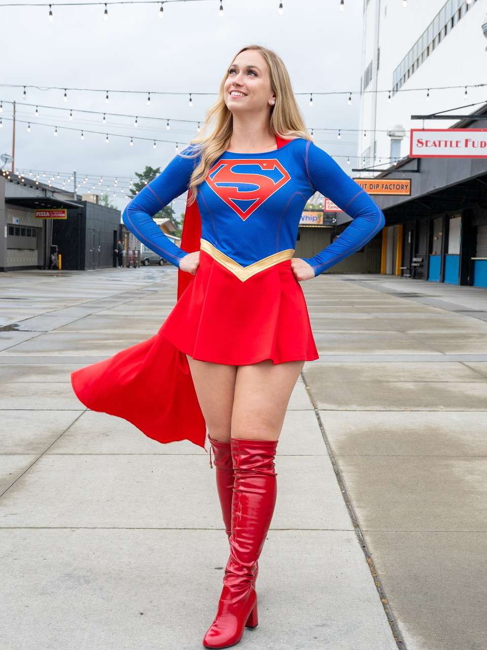 Blonde woman in Supergirl cosplay costume posing outdoors with hands on hips