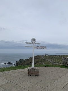 White signpost at a coastal viewpoint above cliffs and the sea on a cloudy day.