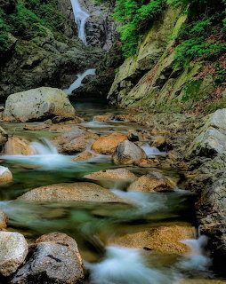 Waterfall cascading into a rocky mountain stream with smooth turquoise water and green vegetation