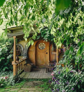 Round wooden door in vine-covered hillside with wooden deck and lantern, fairy tale cottage style