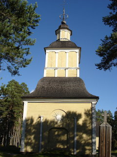 Yellow wooden church tower framed by pine trees against a blue sky