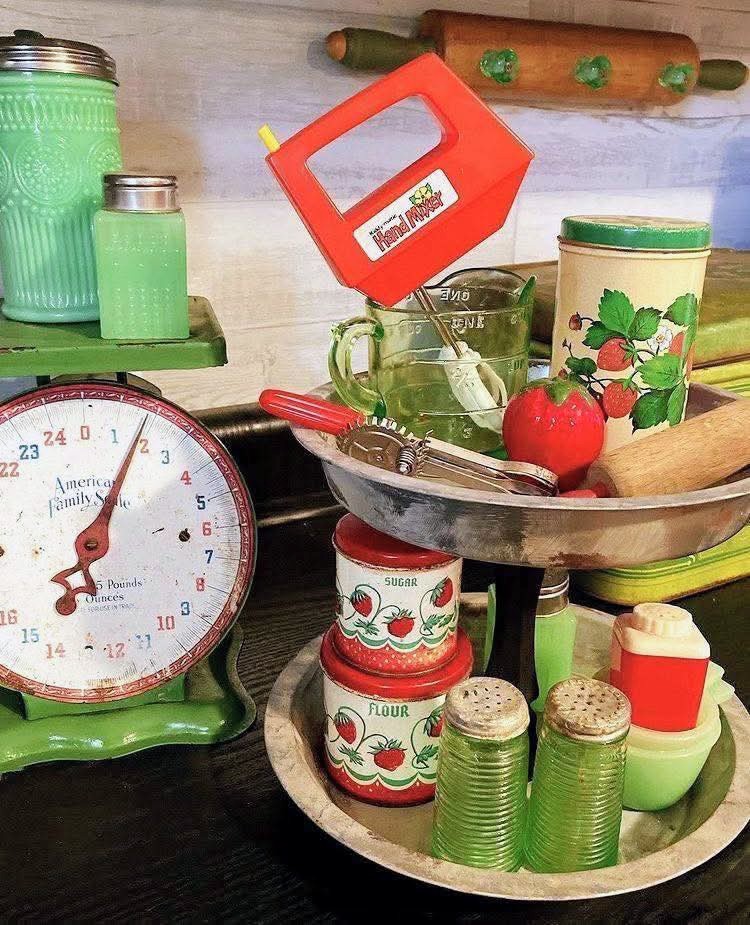Vintage kitchen display with jadeite green glassware, strawberry tins, retro scale, and toy mixer on tiered trays