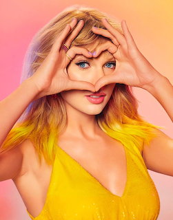 Woman with blonde hair making a heart shape with her hands over her eye, wearing yellow against gradient background