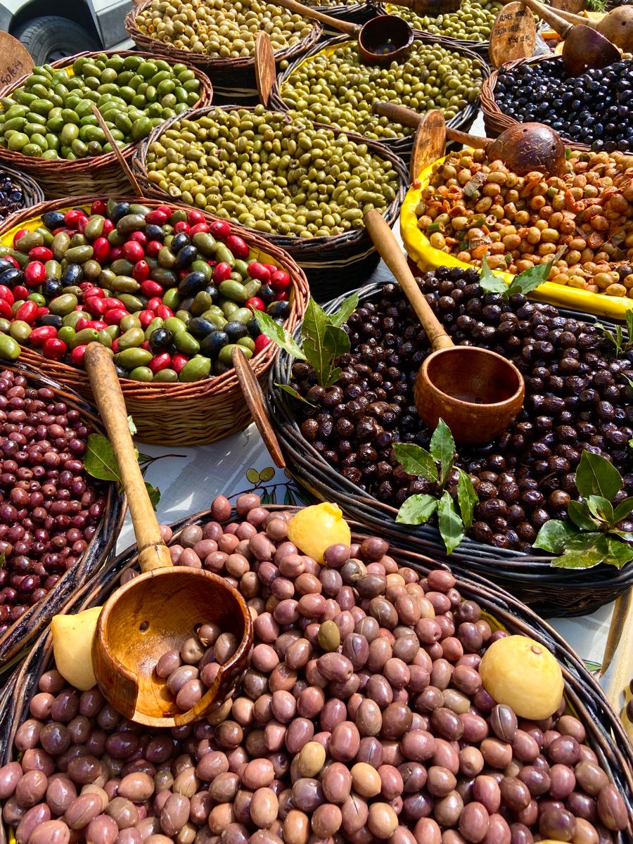 Variety of colorful olives displayed in wicker baskets at a market with wooden scoops