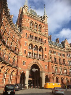 Red brick Victorian Gothic St Pancras railway station with clock tower under blue sky