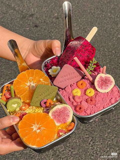 Hand holding metal tray with three decorated fruit popsicles featuring dragon fruit, orange, kiwi and fig slices