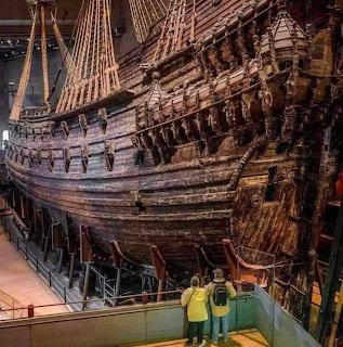 Historic wooden Vasa warship displayed indoors with two visitors standing in front