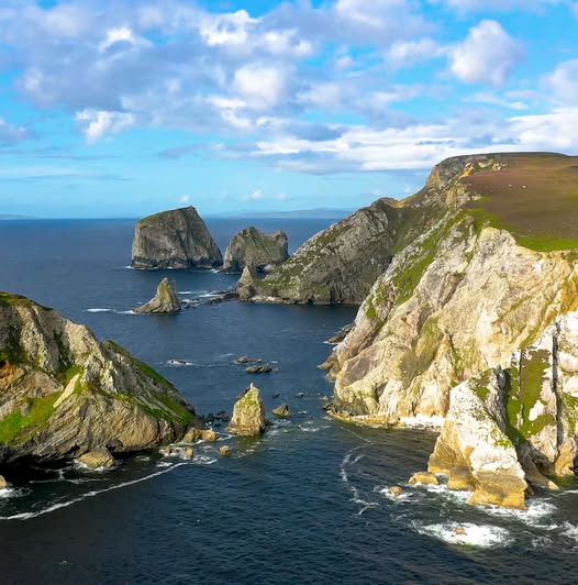 Rocky coastal cliffs and sea stacks above blue ocean under a cloudy sky