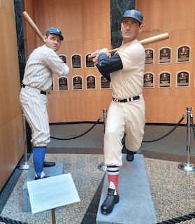 Two life-size baseball player statues in batting stances at the Baseball Hall of Fame with plaques on wall