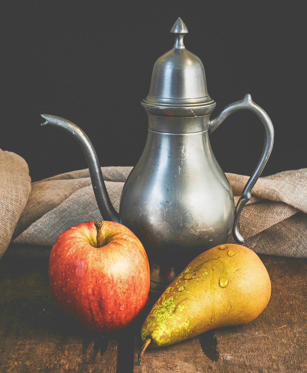 Still life of a pewter jug with an apple and pear on a wooden table