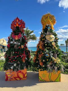 Two festive Christmas trees decorated with tropical ornaments standing on a sunny beach with ocean view
