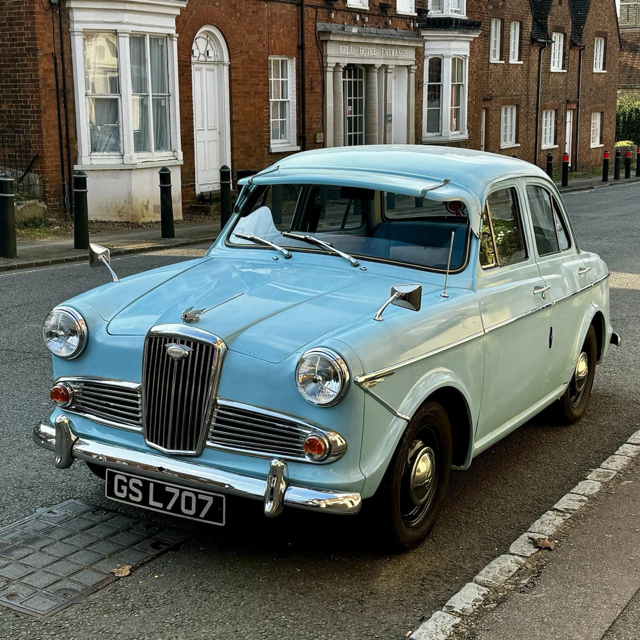 Vintage two-tone turquoise and cream Wolseley 1500 car parked on cobblestone street with brick buildings behind