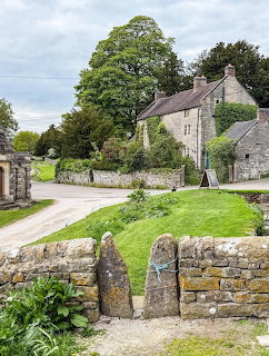 Stone cottages beside a country lane with a large tree and stone wall in an English village