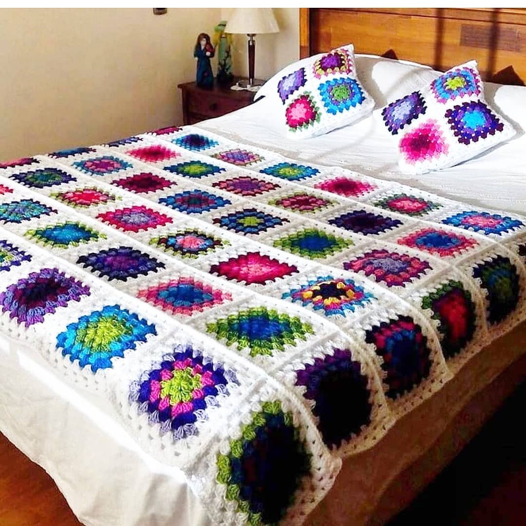 Bed with colorful crocheted granny square blanket and matching pillows in a bedroom