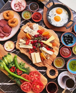 Overhead breakfast spread with eggs, meats, cheese platter, vegetables, and pastries on wooden boards