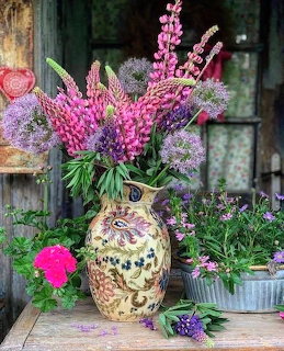Ornate ceramic vase with pink lupins and purple alliums on a rustic wooden porch table