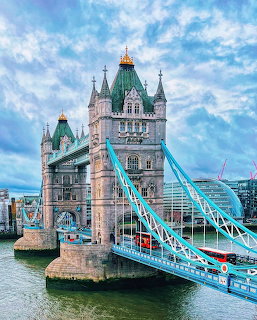Tower Bridge in London with blue suspension cables over the River Thames under cloudy skies