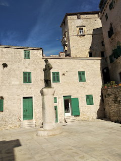 Stone plaza with statue in Šibenik old town, Croatia, surrounded by historic buildings with green shutters