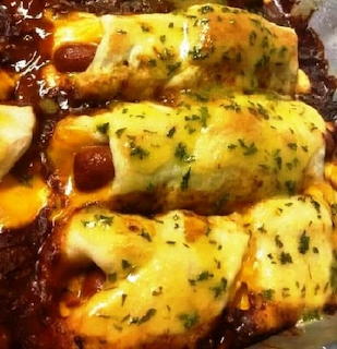 Hot dogs wrapped in dough covered with chili, melted cheese and herbs