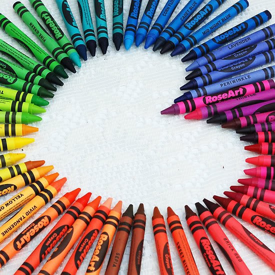 Crayons arranged in a circular rainbow pattern on white surface