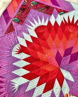 Colorful handmade quilt with red starburst center and pink purple patchwork border