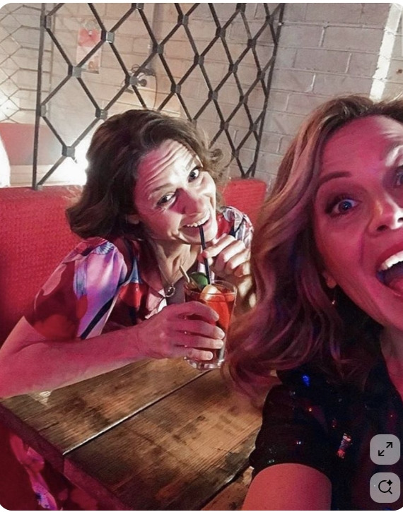 Two laughing women holding cocktails at a restaurant booth with red seating