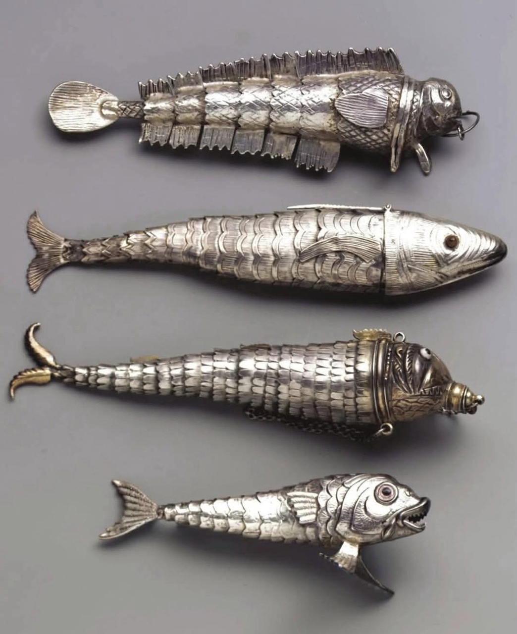 Four silver fish-shaped decorative objects on a gray background