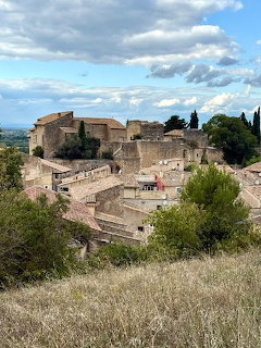 Historic stone hilltop village with terracotta roofs surrounded by greenery under cloudy sky