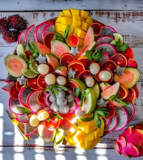 Circular arrangement of sliced tropical fruits including dragon fruit, mango, watermelon, and citrus on a white table