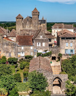 Medieval stone castle with towers overlooking a historic French village with traditional houses and green landscape