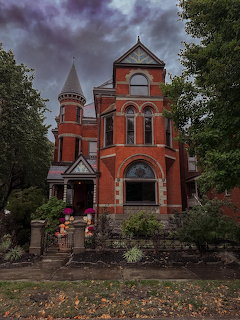 Victorian red brick mansion with turrets and arched windows surrounded by trees under stormy sky