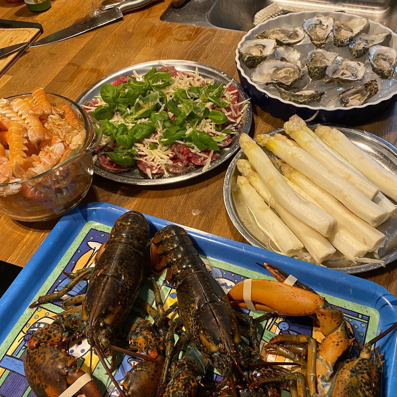 Seafood spread with lobsters, oysters, salad, smoked salmon, and white rolls on a wooden table