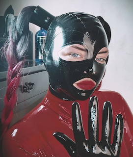 Woman in black latex hood with pigtails and red latex gloves posing indoors