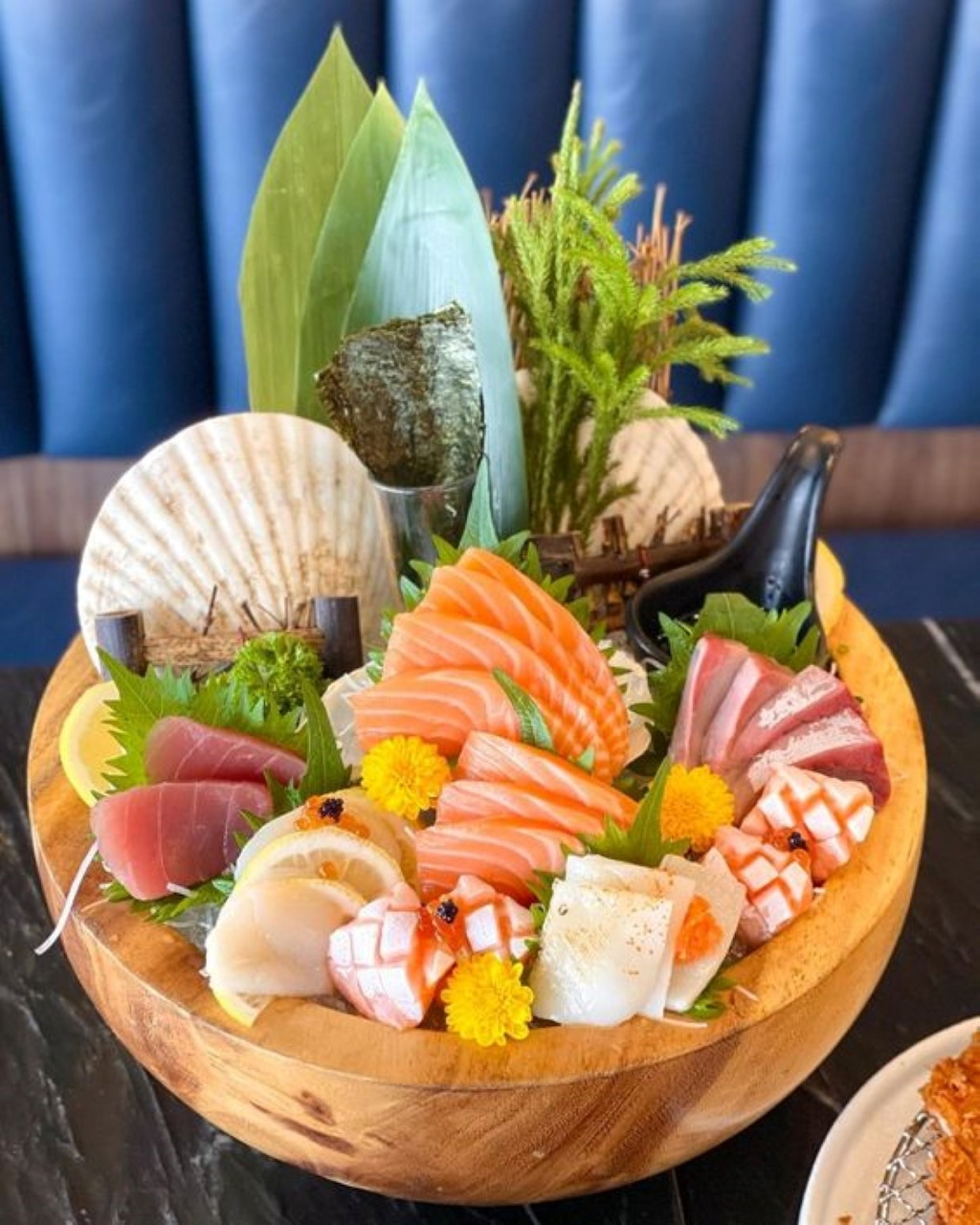 Wooden bowl with assorted sashimi, shellfish, seaweed and edible flowers in artistic arrangement