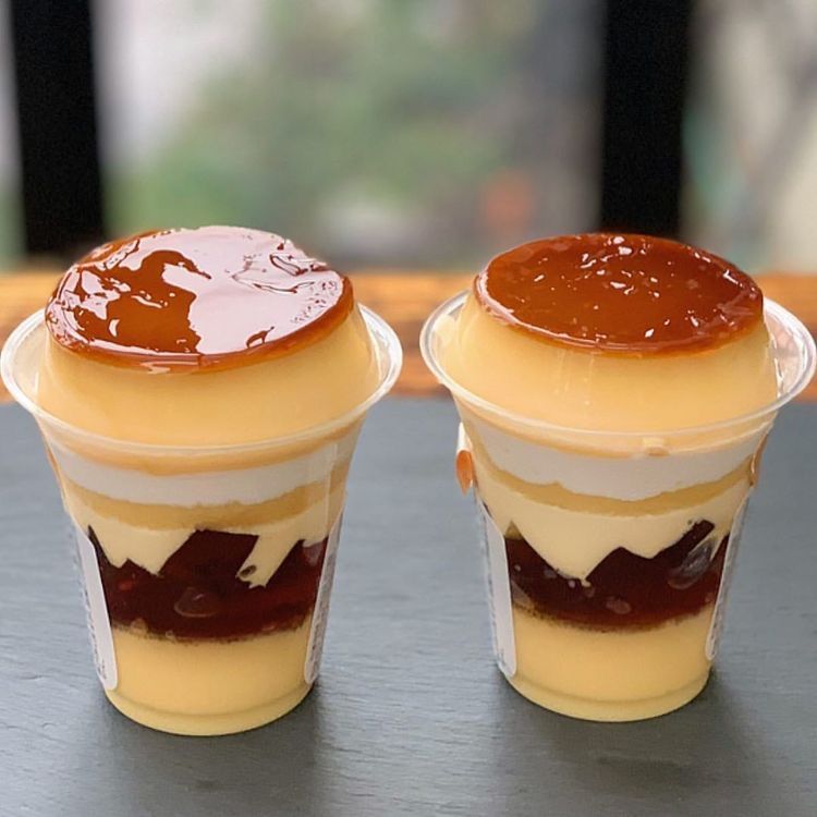 Two cups of layered Japanese pudding with caramel topping on a dark table