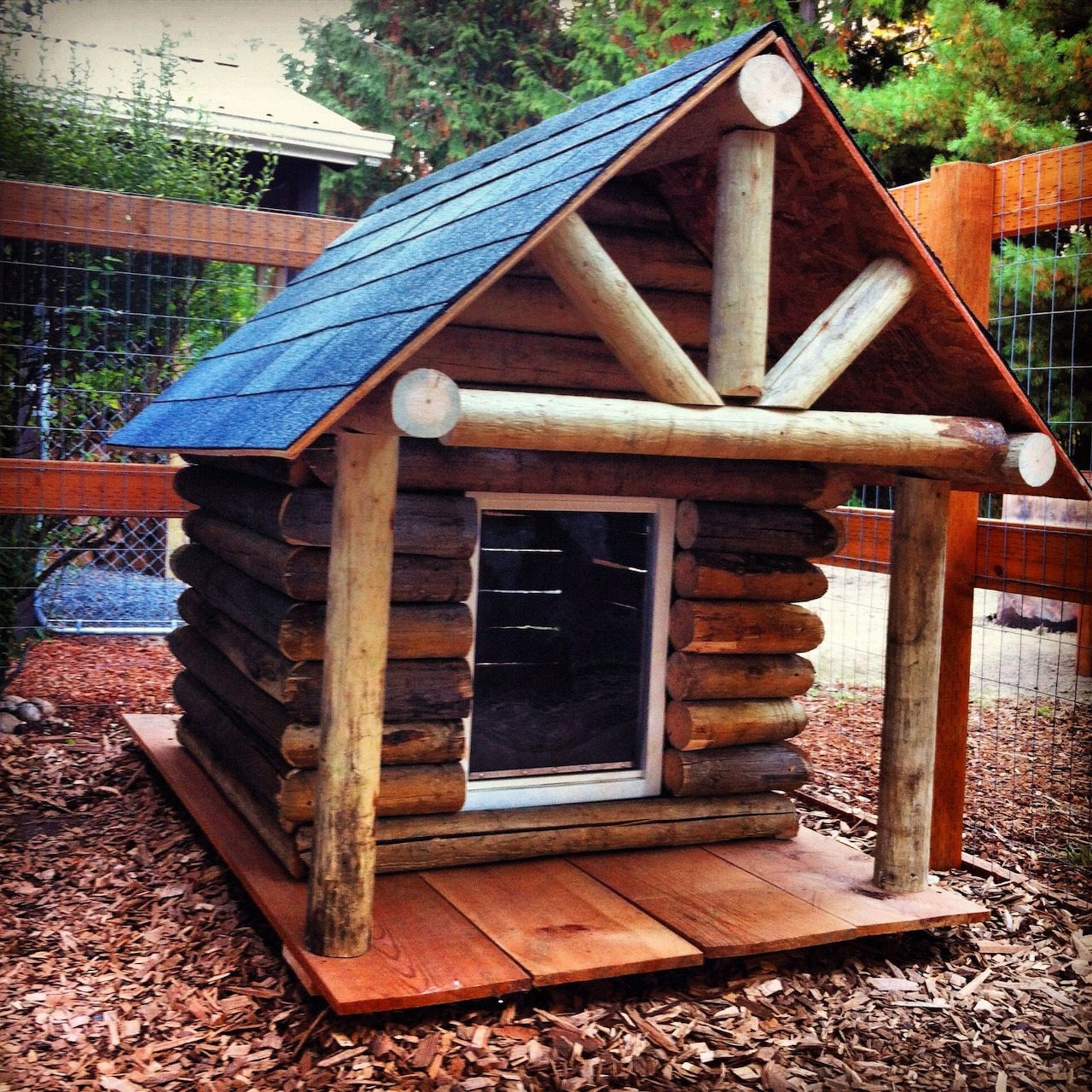 Rustic log cabin doghouse with blue roof and wooden porch in backyard