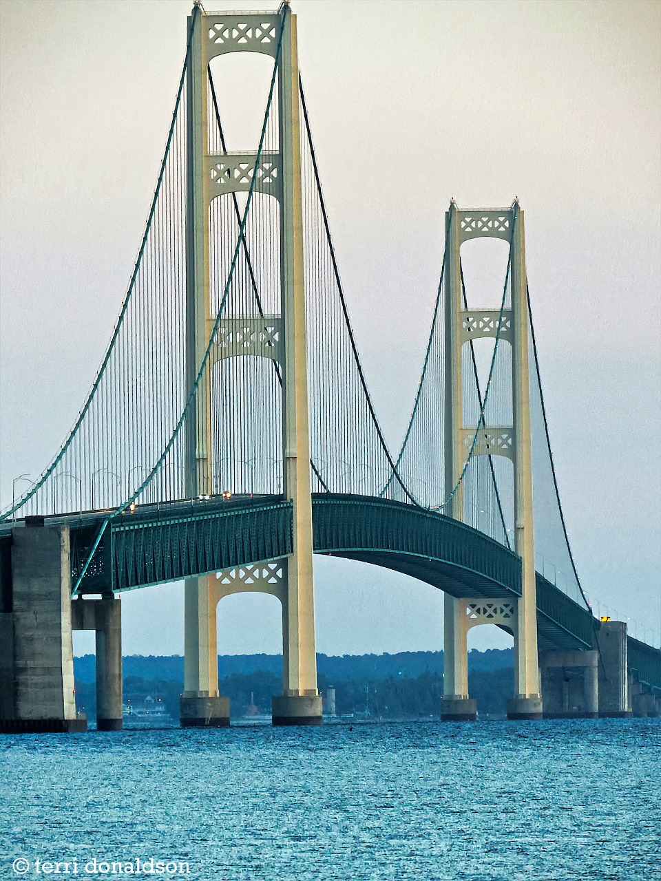 Mackinac Bridge suspension towers rising over blue water under a pale sky