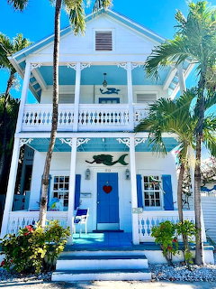 White tropical house with blue trim, balcony, palm trees and red heart on door