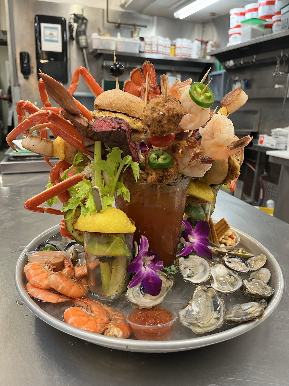 Elaborate Bloody Mary with seafood, pickles, and garnishes towering from a glass on a platter
