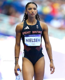 Female Great Britain track athlete in a navy competition uniform walking on the field