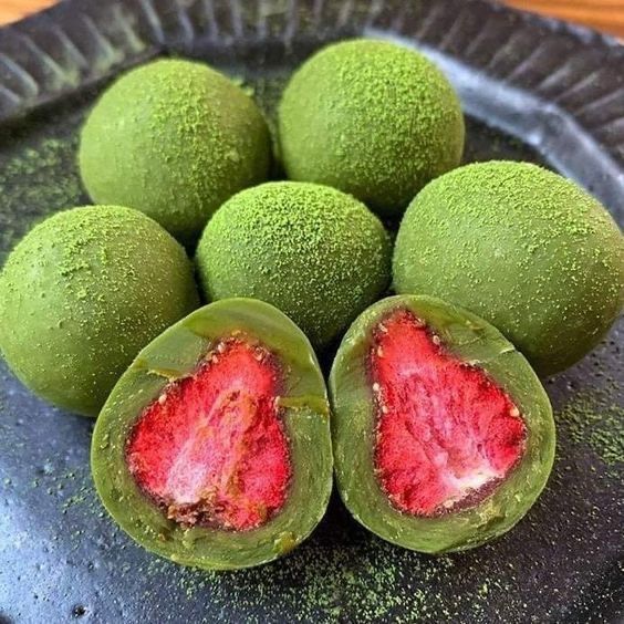 Matcha-dusted strawberries on dark plate, two halved showing pink fruit inside
