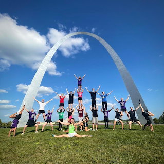 Circus troupe doing acrobatic formations on grass in front of the Gateway Arch in St. Louis