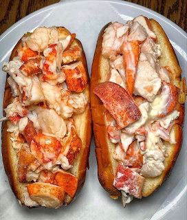 Two lobster rolls filled with chunky lobster meat on toasted buns on a white plate