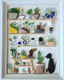 Framed sea glass art with colorful pieces arranged on shelves depicting plants, cats, and vases