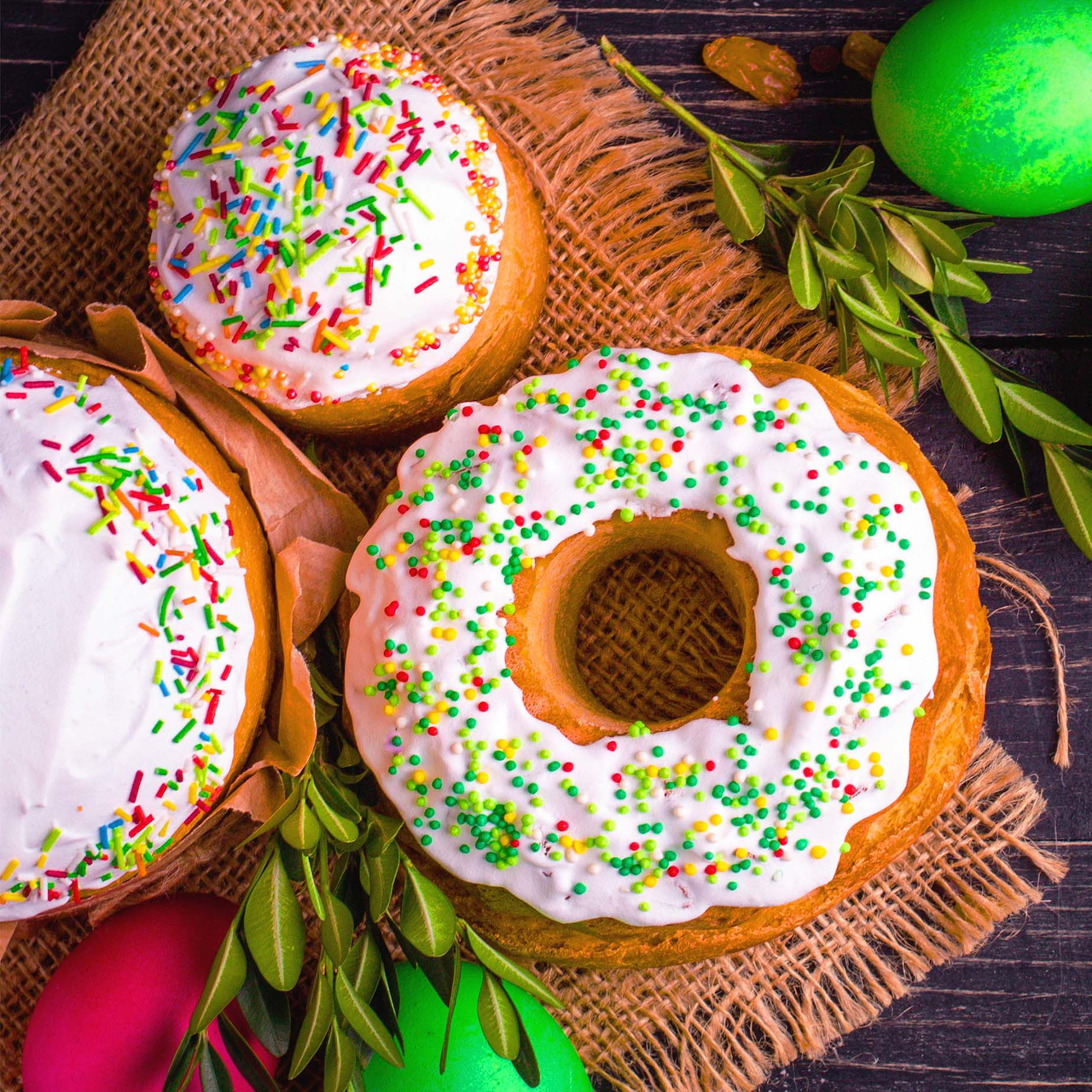 Three frosted donuts with colorful sprinkles on woven mat with cinnamon sticks and tulips